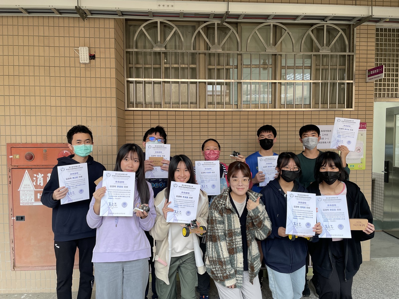 2025/01/22 國立臺灣師範大學 AI 晶片小車實作工作坊結業，手持研習證明，桌上為 AMB82 自駕小車。