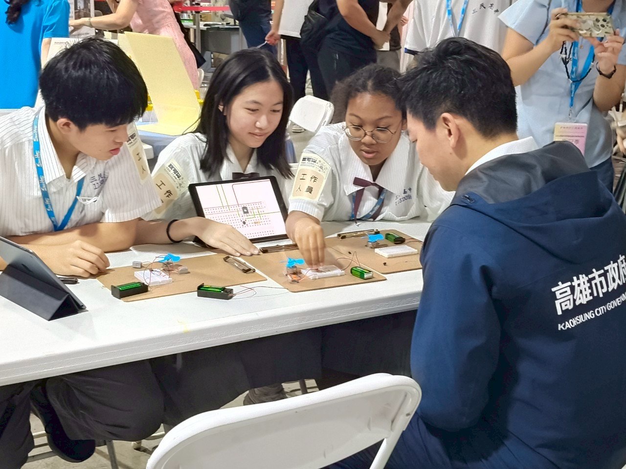 手持平板展示電路架構圖，同步示範實體麵包板的運作。